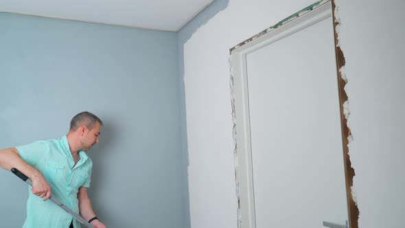 A Man Uses a Paint Roller to Paint the Wall Gray