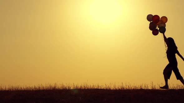 A Girl with Balloons Runs Against the Background of the Sunset, Silhouette