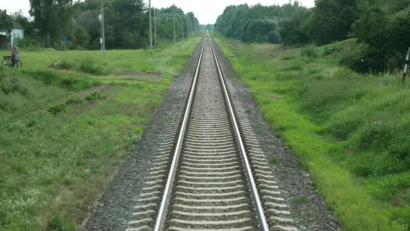 Train is moving on rails and passing meadows, village, bridge