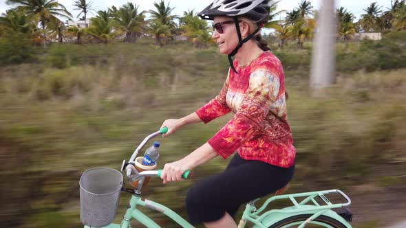 Closeup of laughing mature woman riding a cruiser bike on a tropical vacation.