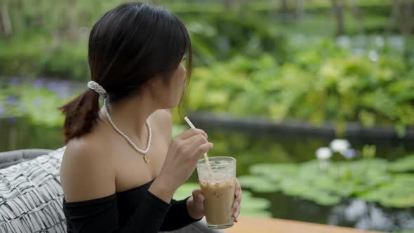 Portrait Shot of Beautiful Young Asian Woman Drinking Cold Coffee in a Green Nature Background