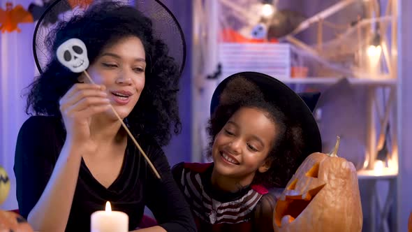 Little Girl and Woman African American in Witch Hat Laugh and Light Candle in Pumpkin with Carved