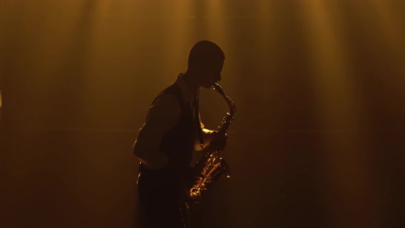 Silhouette a Young Stylish Guy Plays the Golden Shiny Saxophone in the Yellow Spotlights on Stage