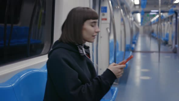 Happy Woman in Earphones Sitting at Metro and Using Mobile