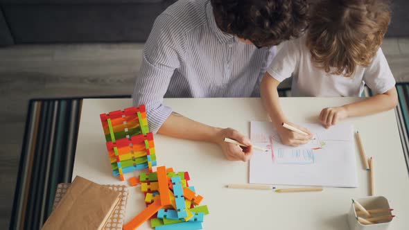 Little Kid Drawing and Colouring Picture with Careful Mother at Table at Home