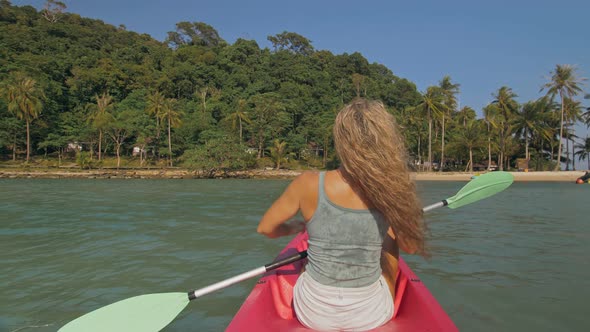 Long Haired Blonde Woman with Sunglasses Rows Bright Pink Canoe Along Sea Bay Water to Beach with