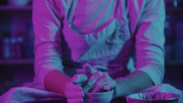 Young Woman Potter Working in the Studio in Neon Lighting  Smears Her Face with Clay