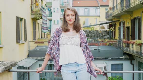 Pretty woman leaning on balcony railing, looking at camera