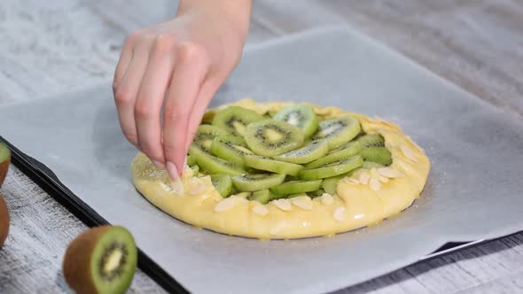 Female hands making galette with fresh kiwi. Sprinkle with almond petals.