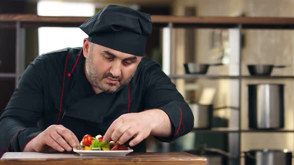 Confident Bearded Male Chef Putting Tomatoes on Vegetable Mix