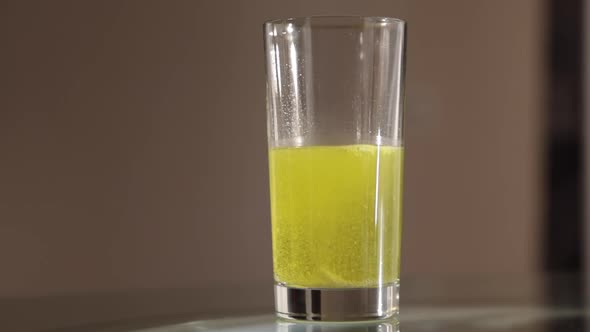 Effervescent yellow tablet dissolves in a transparent glass of water close-up