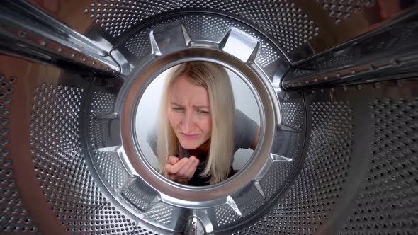 Young blonde looks inside washing machine, smells stench and plugs her nose