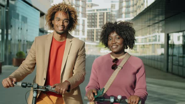 Portrait of Smiling Afro Man and Woman with E-Scooters in City