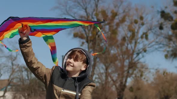 A Happy Boy with a Flying Rainbow Kite Rides a Bicycle on the Road