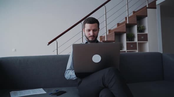 Man Is Sitting on Sofa and Working Using Wireless Laptop