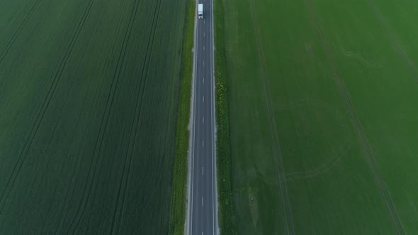 Truck Driving on Asphalt Road Between Bright Green Fields Aerial View