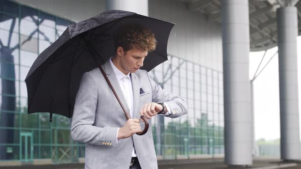 Handsome Business Man Waiting for Taxi Driver Near Airport Entrance Standing with Umbrella Looking