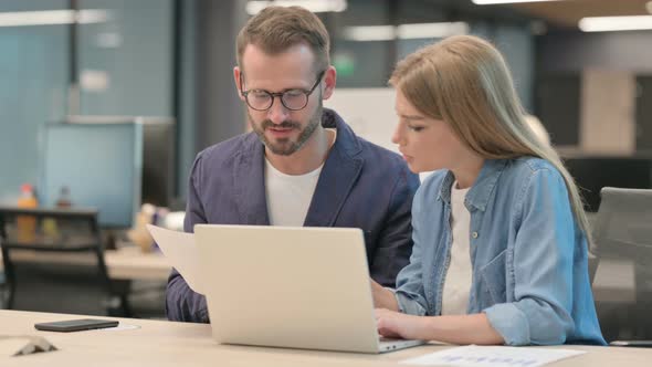 Businessman and Businesswoman Reading Documents While Using Laptop