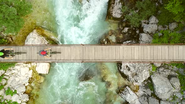 Aerial view of couple crossing a wooden bridge on bicycles at the Soca River.