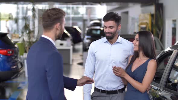 Joyful Couple Taking Key To Bought Car at Showroom