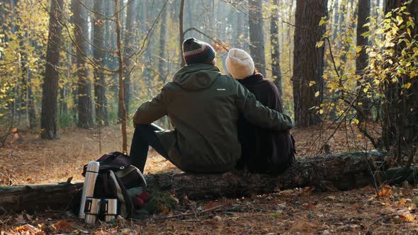 A Couple of Tourists Sitting on a Log, Resting in the Autumn Forest