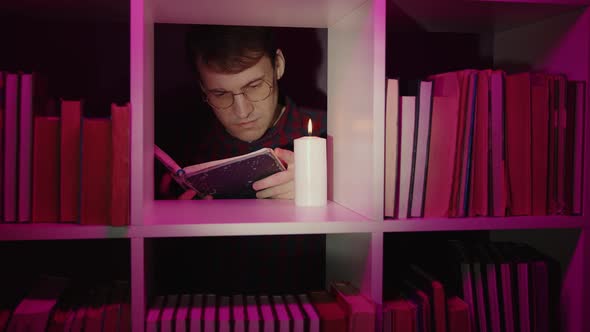 Serious Man Reading Book Near Candle in Bookcase