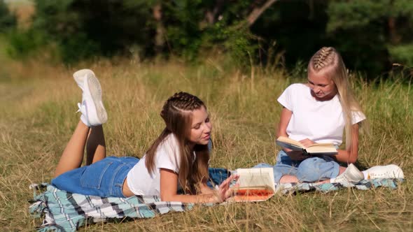Two Beautiful Girlfriends are Reading Books Relaxing on a Blanket in Nature