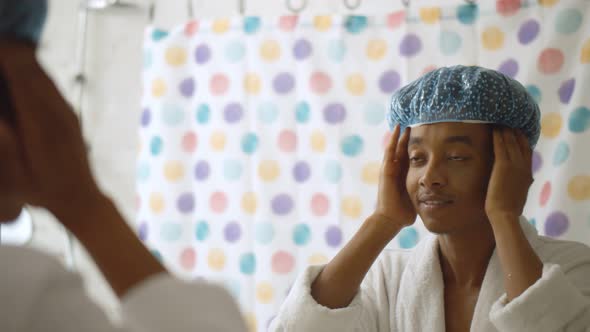 Young African Man in Bathrobe Looking Into Mirror Putting on Shower Cap Before Taking Bath