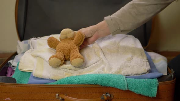 Parent packing suitcase with clothes and teddy bears medium shot