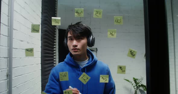 Young Man Listens to Music in Headphones and Planning on the Glass Wall
