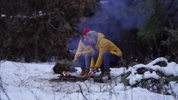 Young Man and Woman Near a Campfire in the Forest in Winter