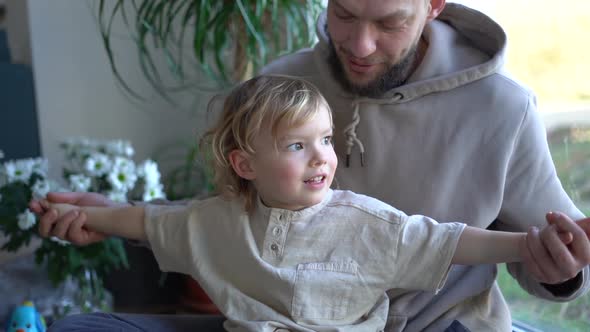 Happy Cheerful Caucasian Man Hugging His Small Cute Son and Laughing at Home