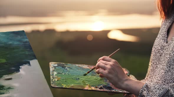 A Young Woman Artist Mixing Green and Blue Oil Paints on the Palette at Sunset