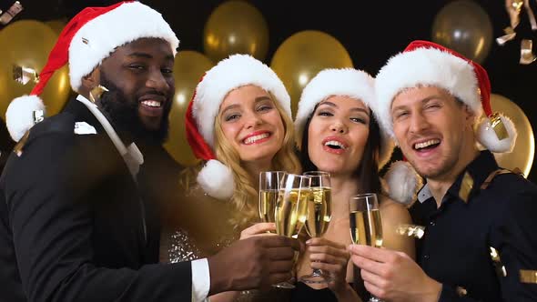 Smiling Friends in Santa Hats Clinking Champagne Glasses Under Falling Confetti