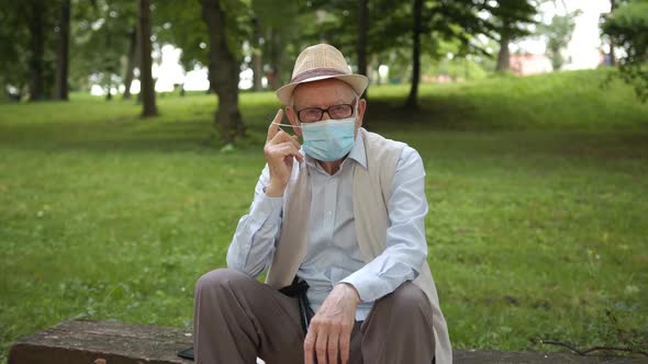 Portrait of an Old Man Sitting on a Park Bench and Taking Off a Medical Mask
