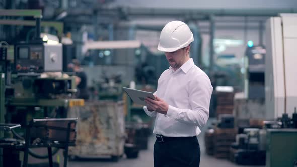 Engineer in Hard Hat is Moving Through a Heavy Industry Factory with a Tablet Computer