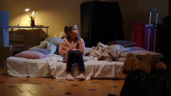 Wide Shot Scared Girl Running to Mattress in Bomb Shelter Looking Away Hearing Bombardment