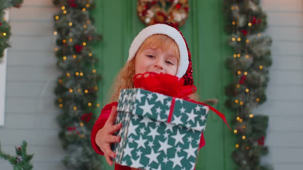 Happy Toddler Child Girl Kid in Red Sweater Gifting One Christmas Present Box Stretches Out Hands