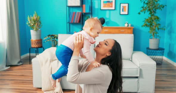 Loving Mother Sits on Carpet Grabs Baby Tightly and Lifts It on Her Outstretched Arms