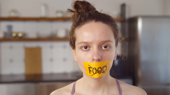 Young Woman with Stick Tape with Crossed Out Word Food Covering Mouth Standing at Home