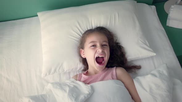 Portrait of a Happy Cute Funny Cheerful Little Child Girl in White Pajamas Wakes Up in Bed in the