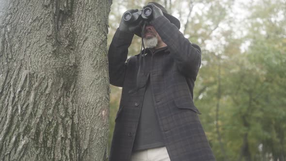 Middle Shot of Concentrated Serious Detective or Intelligence Agent Using Binoculars for Spying