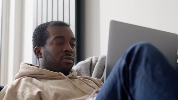 Young Man Relaxing At Home Lying On Sofa Using Laptop To Work From Home Or Shop Online