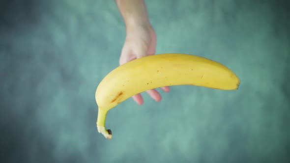 Hand Throws Up and Catches Ripe Yellow Banana Above Table