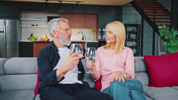 Happy Middle Aged Adult Married Couple Drinking White Wine From Glasses While Sitting on Sofa
