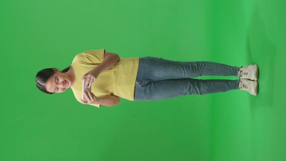 Full Body Of Smiling Young Asian Kid Girl Looking At The Phone Screen On Green Screen alt