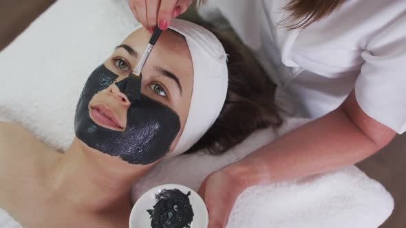 Caucasian woman lying back while beautician gives her a face mask