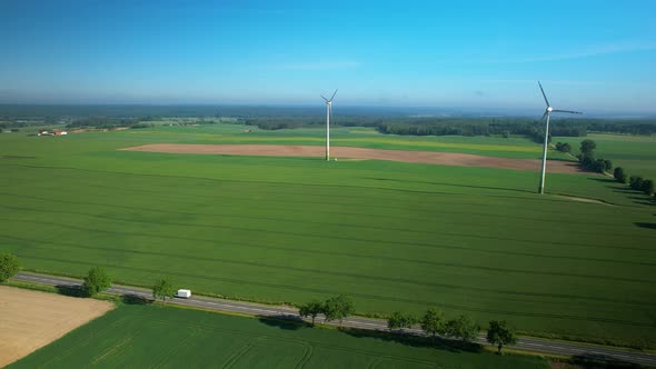 Aerial Panorama Of Green Field And Wind Turbines With Isolated Road.