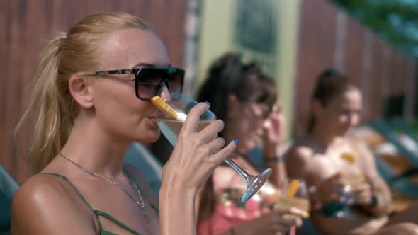 Beautiful tanned girls drink cocktails on sunbeds by the pool	