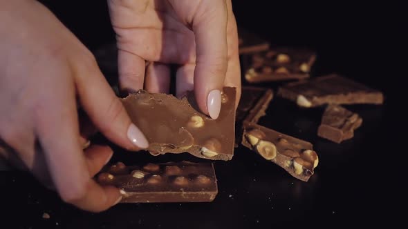 Woman Breaks Black Chocolate Bar with Nuts